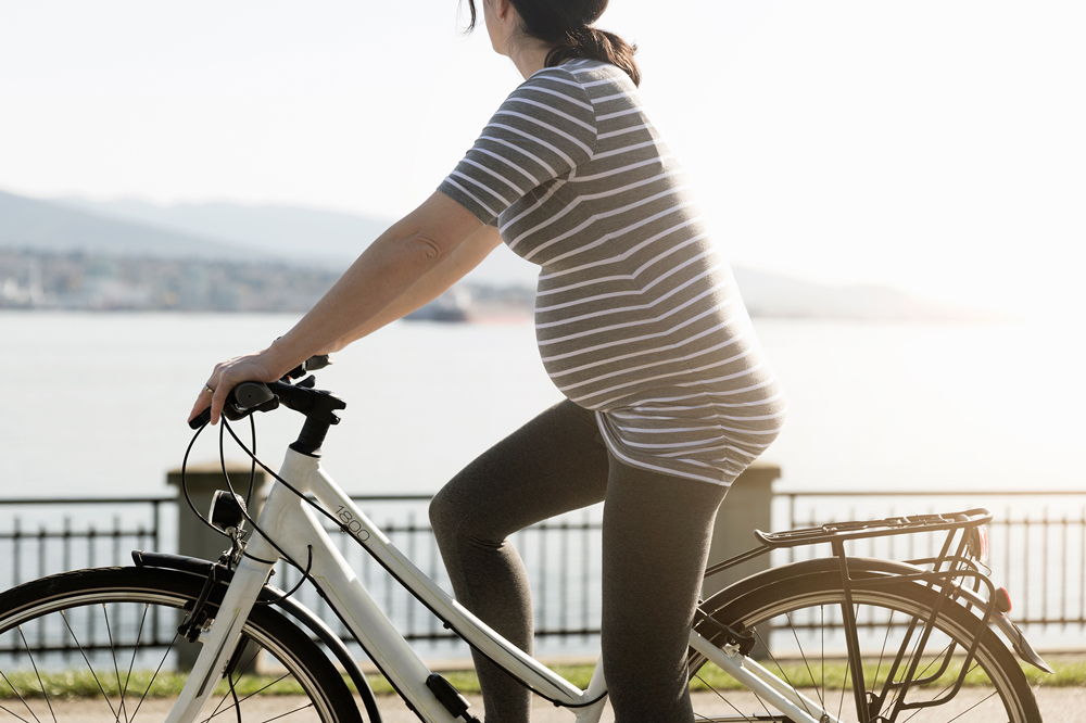 Беременная девушка на велосипеде едет по набережной