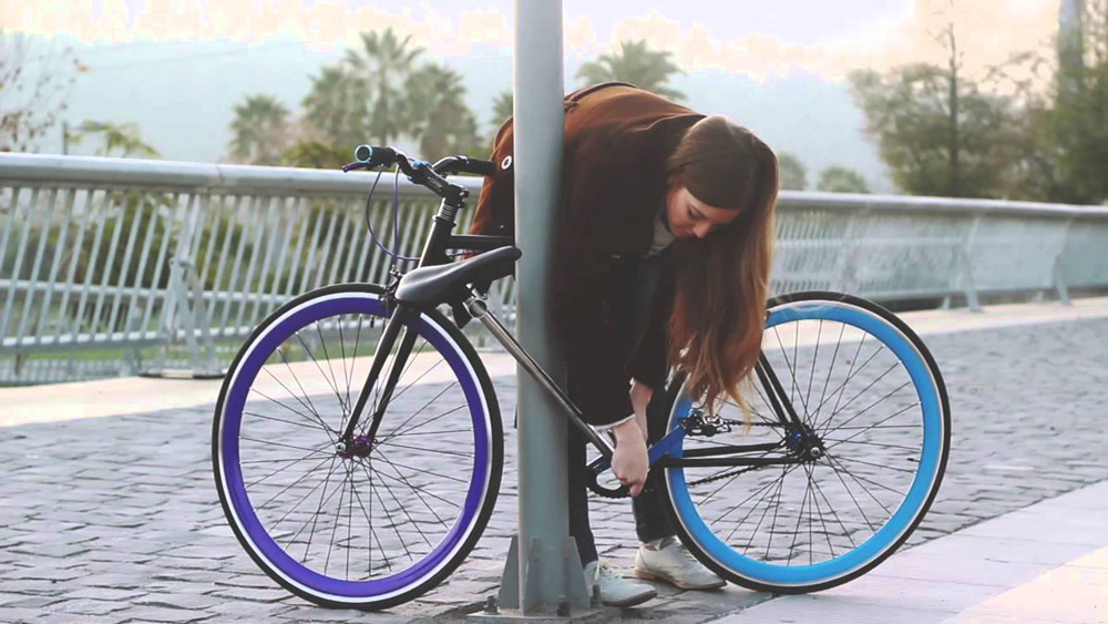 Девушка пристегивает велосипед к столбу