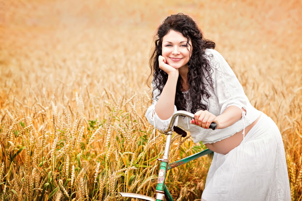 Беременная женщина с велосипедом в поле