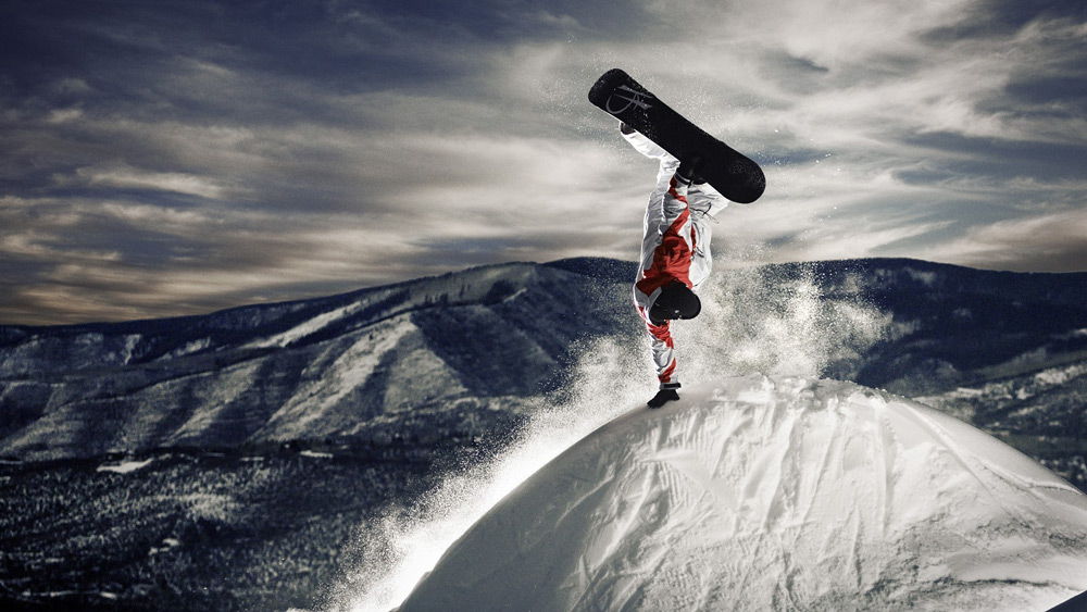 Человек выполняет трюк на сноуборде на вершине горы