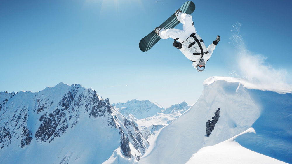 Человек выполняет трюк на сноуборде в горах